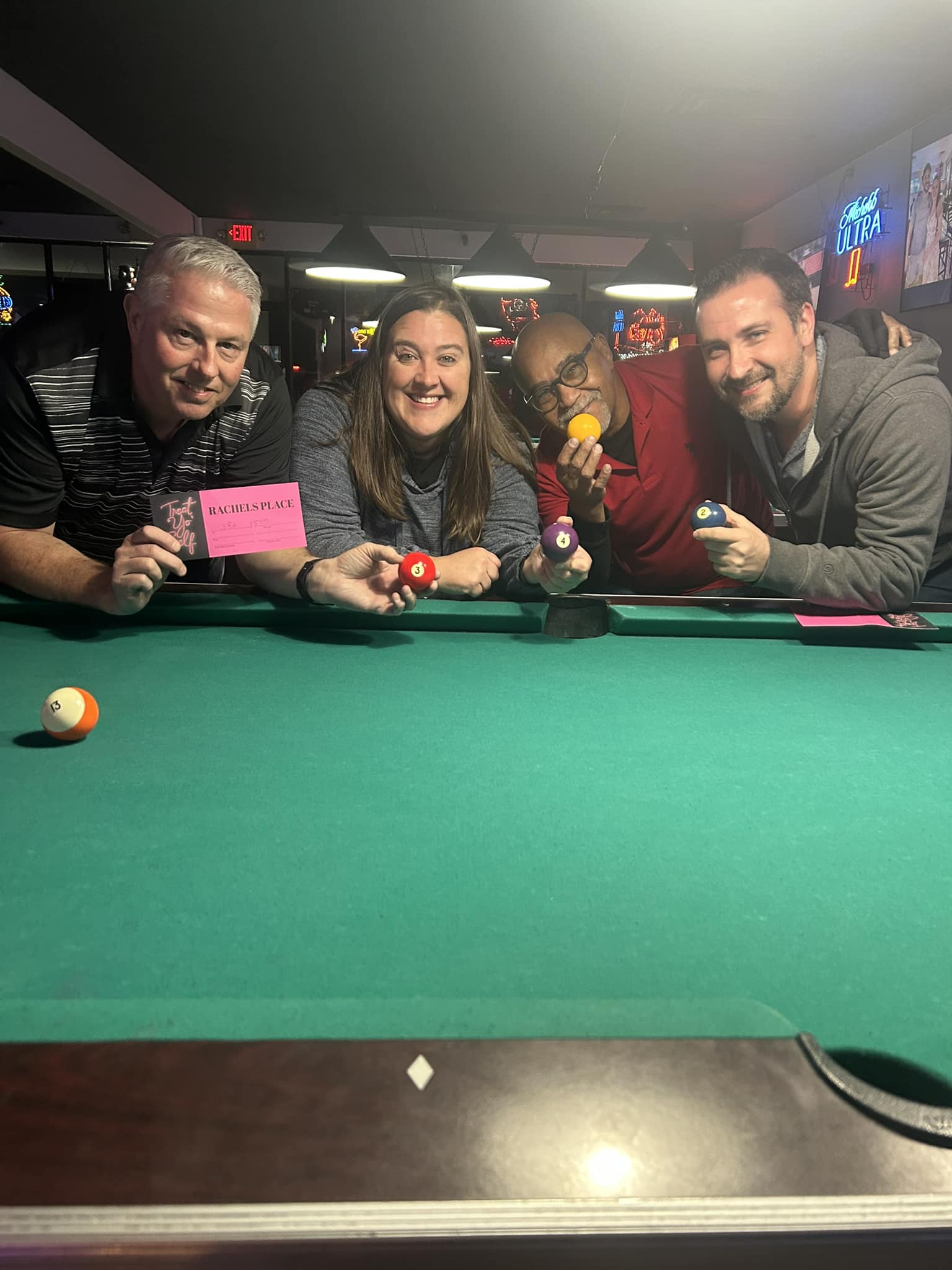 A group of cash-tournament winners holding cues at the pool table.